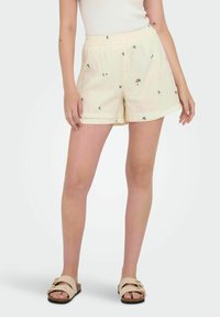 Pantalones cortos amarillos claros con un acabado texturizado, que presentan un pequeño bordado floral verde, cinturilla elástica y bolsillos laterales.
