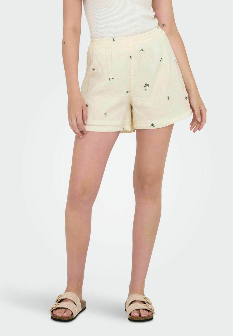 Pantalones cortos amarillos claros con un acabado texturizado, que presentan un pequeño bordado floral verde, cinturilla elástica y bolsillos laterales.