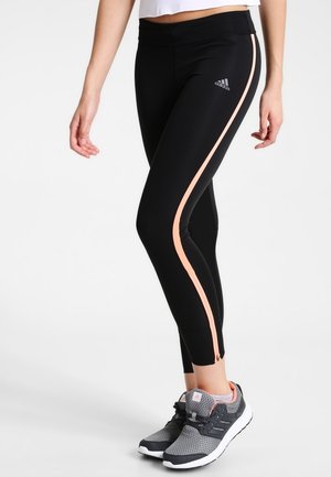 Zwarte sportleggingen met een aansluitend ontwerp, voorzien van roze zijkanten en een logo. Gecombineerd met grijze sportschoenen met gaasaccenten.