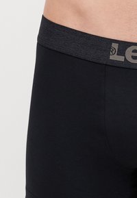 Svarta boxershorts med ett mörkgrått elastiskt midjeband som har en logo. Tyget verkar slätt och åtsittande.