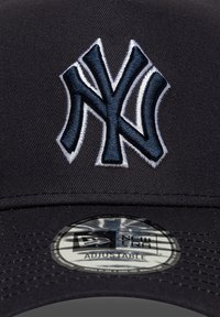 Svart baseballcaps med et hevet, brodert marinen blått og hvitt NY-logo. Har en strukturert krone og en justerbar stropp. New Era-merke klistremerke festet.