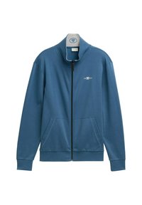 Blå zip-up jakke lavet af glat stof. Har høj krave, to forlommer og et lille logo på venstre side.