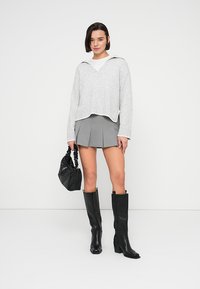 Γκρι πλεκτό πουλόβερ με V-λαιμόκοψη, συνδυασμένο με γκρι πλισέ φούστα. Μαύρες δερμάτινες μπότες μέχρι το γόνατο και μια μικρή μαύρη τσάντα συμπληρώνουν το ντύσιμο.