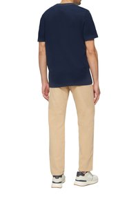 Marineblauw katoenen T-shirt met korte mouwen, gecombineerd met beige broek. Witte sneakers met marineblauwe en grijze accenten maken de outfit compleet.