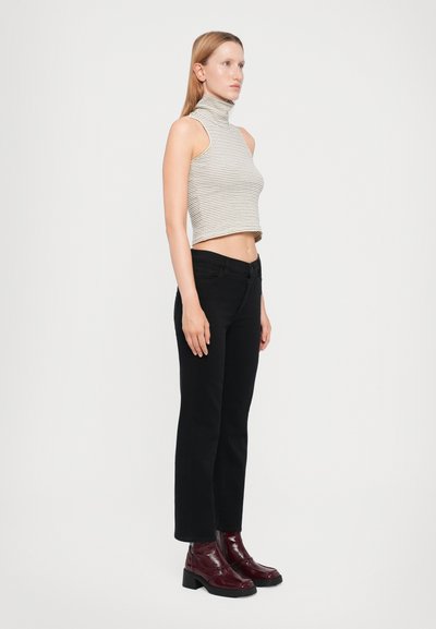 Top halter cropped a righe beige e bianco, abbinato a jeans dritti neri e stivali alla caviglia borgogna lucidi con tacco spesso.