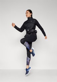 Black athletic jacket with a textured pattern, black leggings with colorful graphic accents, and blue running shoes.