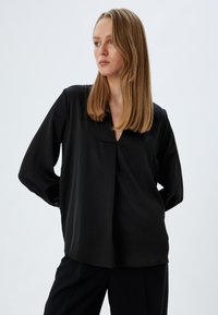 Sort, langærmet bluse lavet af glat stof. Har en V-udskæring og en diskret plissering foran, løs pasform og minimalistisk design.