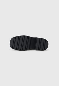 Sort gummisåle med en tekstureret overflade, der har vandrette riller og en rund tå. Simpelt, holdbart design til godt greb.