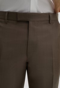 Braune maßgeschneiderte Hose aus glattem Stoff, mit flachem Vorderteil, Gürtelschlaufen und subtilen Nähdetails.