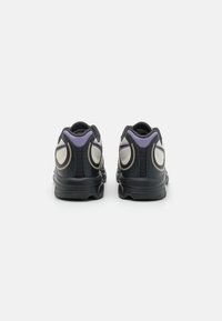 Sapatos athletic pretos com um acabamento texturizado, apresentando um acento roxo e detalhes de design curvados no calcanhar. Sola de borracha sólida.