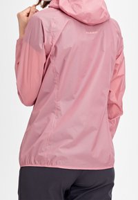 Lehká růžová voděodolná bunda s kapucí, s elastickými manžetami a stahovacími lemy. Logo značky viditelné na zadní straně.
