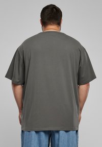 Graues oversized Kurzarm-T-Shirt aus weichem Stoff, mit rundem Halsausschnitt und geradem Saum, von hinten betrachtet.