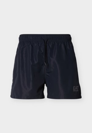 Marineblå badeshorts laget av lett, glanset stoff med elastisk midje og justerbar snor. Har en logo trykt på siden.