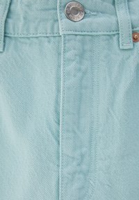 Gros plan d'un tissu en denim bleu clair avec des coutures visibles, un bouton en métal et une passants de ceinture.