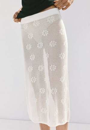 Persona con falda de punto blanca translúcida con estampados florales sobre una capa base sólida blanca, combinada con un top negro.