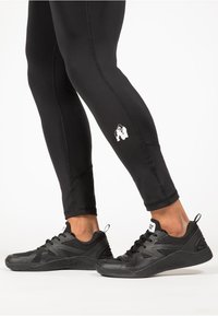 Zwarte sportleggingen met een aansluitend ontwerp en een wit logo, gecombineerd met zwarte sneakers met een gestructureerd mesh bovenwerk en een rubberen zool.