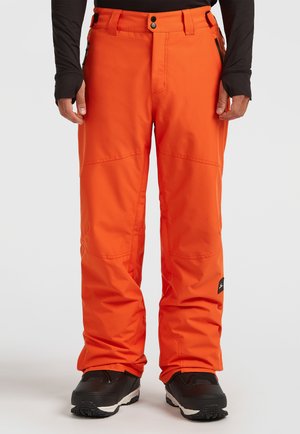 Oranje sneeuwbroeken met een recht model, meerdere zakken en versterkte naden, gecombineerd met zwarte sneeuwlaarzen. Duurzaam materiaal.