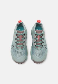 Paar lichtblauwe hardloopschoenen met patroonkoordjes, geperforeerde mesh bovenkant, rode trekbandjes en "ZEGAMA"-tekst op de tong.