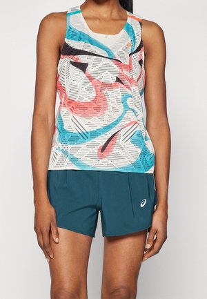 Femme portant un débardeur blanc sans manches avec des motifs abstraits roses, bleus et noirs, et un short de sport bleu sarcelle foncé avec un logo.