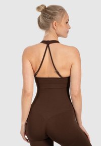 Hnědý žebrovaný body s přiléhavým střihem, který má nastavitelné ramínka a styl racerback, zvýrazňující hladkou strukturu.