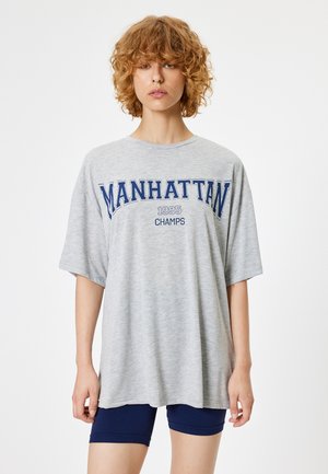 Szary, oversize T-shirt z napisem "MANHATTAN 1995 CHAMPS" w kolorze niebieskim. Krótkie rękawy, okrągły dekolt i miękka faktura materiału.