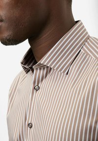 Gestreiftes Hemd aus hellbraunem und weißem Stoff, mit spitzem Kragen, zwei schwarzen Knöpfen und glatter Textur sowie einer taillierten Passform.