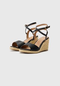 Black wedge sandals with cross-strap design, open toe, textured espadrille heel, and adjustable ankle strap. Smooth leather upper.