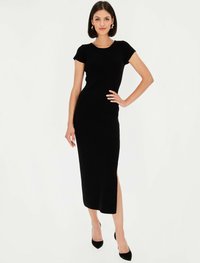 Czarna dzianinowa sukienka z prążkowanego materiału, z krótkimi rękawami, okrągłym dekoltem i wysokim rozcięciem na udzie. Połączona z czarnymi szpilkami i kolczykami w kształcie kół.