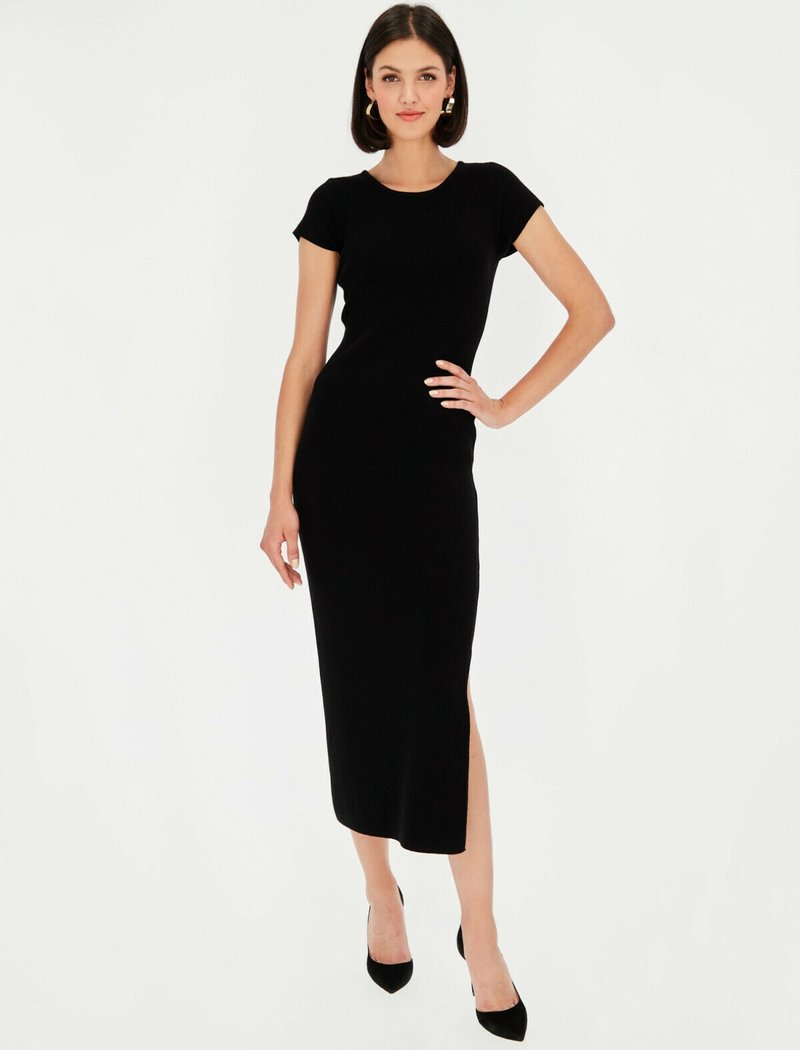 Czarna dzianinowa sukienka z prążkowanego materiału, z krótkimi rękawami, okrągłym dekoltem i wysokim rozcięciem na udzie. Połączona z czarnymi szpilkami i kolczykami w kształcie kół.