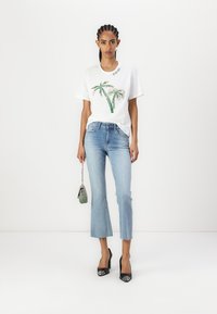 T-shirt bianco in cotone con grafica di palma verde, abbinato a jeans dritti azzurri, e tacchi neri in vernice. Presenta una borsa scintillante.