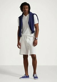 Hvit poloskjorte, hvite shorts, marineblå ermeløs genser drapert over skuldrene, blå joggesko, med klokke på håndleddet.