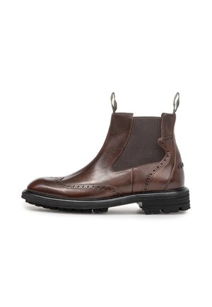Brun læder Chelsea-støvle med brogue-detaljer, sorte elastiske sidelapper, trækflapper og en tyk sort gummisål.