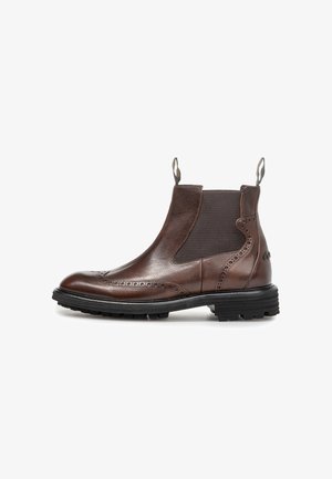 Brun læder Chelsea-støvle med brogue-detaljer, sorte elastiske sidelapper, trækflapper og en tyk sort gummisål.