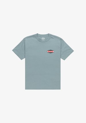 Ljusblå bomulls-t-shirt med korta ärmar, rund halsringning och en röd och svart RVCA-logotyp på vänster sida.