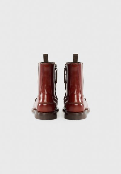 Bottines en cuir bordeaux avec une fermeture éclair sur le côté, des accents élastiques et une semelle brune texturée. Lignes épurées avec un minimum de couture.
