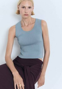Světle modrá žebrovaná cropped top s hladkým materiálem, v kombinaci s tmavě burgundskou zavinovací sukní, která zdůrazňuje čisté linie a textury.
