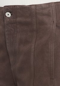 Bruine corduroy tailleband met een zilveren knoopsluiting. Soepele textuur met verticale lijnen en subtiele stiksels, die het casual ontwerp benadrukken.