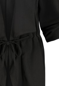 Chaqueta negra estilo kimono con mangas cortas, cintura ajustable y textura de tela suave. Diseño ligero y versátil sin cierres.