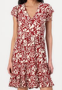 Vestido floral rojo y crema con escote en V, mangas cortas con volantes, costura en la cintura y un dobladillo con volantes en capas. Tejido ligero con un acabado texturizado.