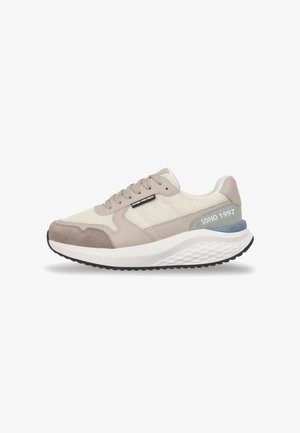 Zapatilla deportiva beige y gris claro con paneles de malla y ante, suela blanca gruesa, dibujo negro en la banda de rodamiento y texto "SOHO 1997" en el talón.