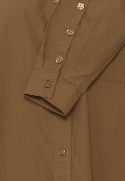 Bruine shirt met een knoopsluiting aan de voorkant, lange mouwen en een gladde textuur. Heeft extra knopen op de manchetten en contrasterende stiksels.