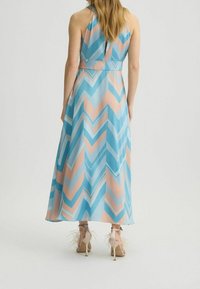 Robe longue à col halter en motif zigzag bleu et rose, réalisée en tissu léger, avec un détail en trou de serrure à l'arrière. Associée à des talons en plumes beige.