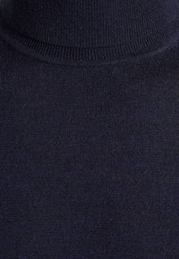 Námořnický modrý rolák vyrobený z měkkého pleteného materiálu, s žebrovaným límcem a hladkou texturou s jemnými barevnými variacemi.