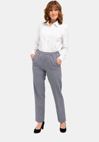 Grijze geruite broek met een elastische tailleband en zijzakken, gecombineerd met een witte overhemd. Zwarte hakken maken de outfit af.