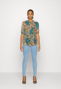 Blusa de manga curta com um padrão floral colorido em azul, rosa e verde sobre um fundo claro; combinada com jeans skinny azul claro.