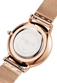 Reloj redondo con caja de acero inoxidable en color oro rosa y correa de malla. La inscripción en la parte posterior incluye detalles de la marca y del movimiento.
