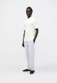 Kurzärmeliges cremefarbenes Poloshirt mit strukturiertem Design, kombiniert mit hellgrauen Hosen und schwarzen Espadrilles mit gewebten Sohlen.