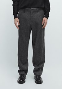 Pantaloni in misto lana grigi con taglio dritto, dotati di frontale piatto, passanti per cintura e chiusura a un bottone, abbinati a scarpe nere.
