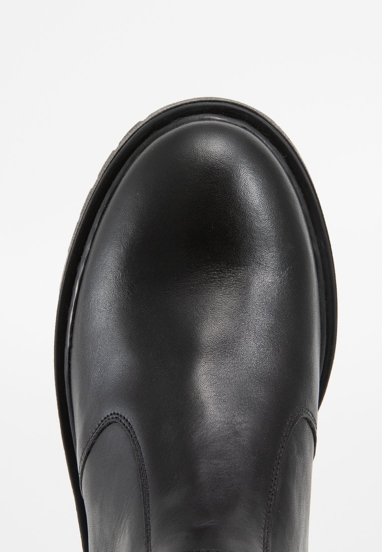 Botte en cuir noir avec un embout arrondi, une texture lisse et des détails de coutures minimaux. La semelle semble épaisse et robuste, adaptée à la durabilité.