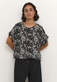 Short-sleeve black and white top with a textured abstract pattern, round neckline, and relaxed fit, paired with black pants.
